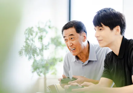 コントローラーで一緒にゲームを楽しむ高齢の男性と若い男性（利用イメージ）