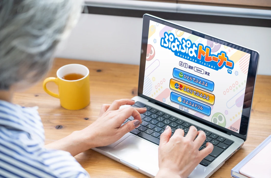 ノートパソコンで「ぷよぷよトレーナー」のモード選択画面を操作している手元（利用イメージ）