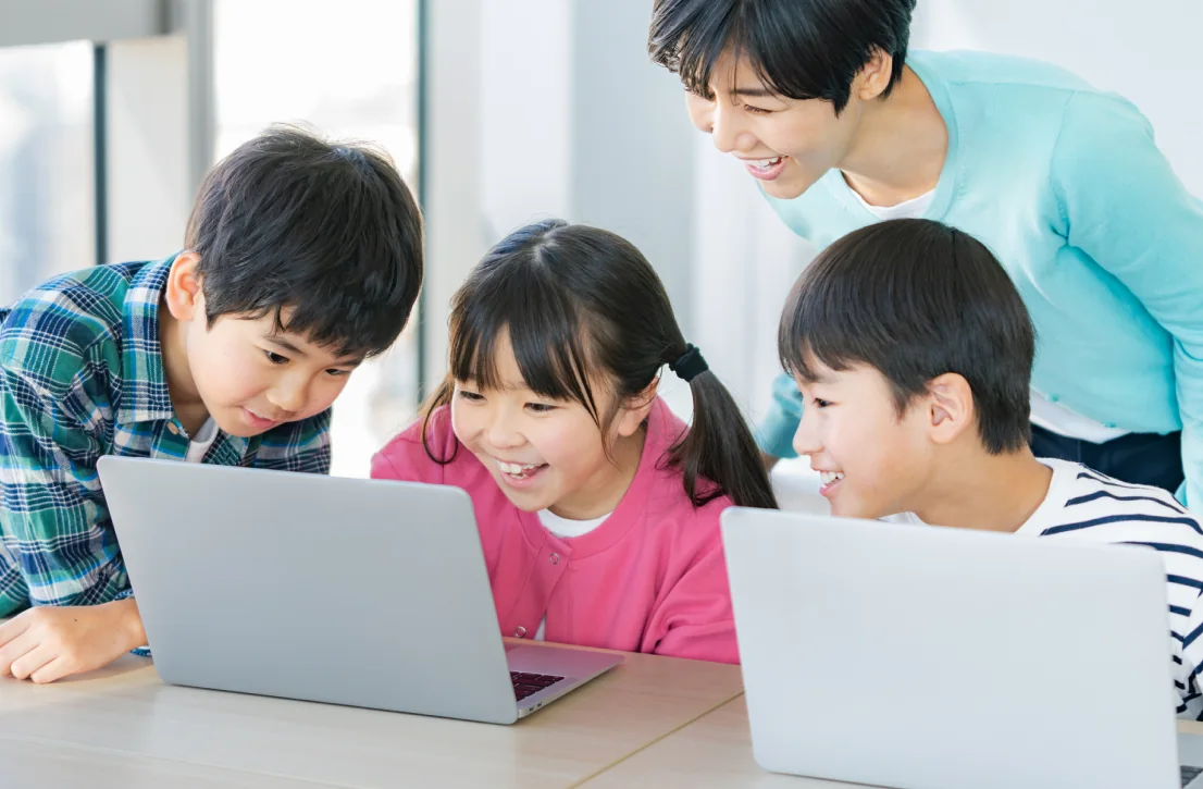 子どもたちがノートパソコンを囲み、職員が見守りながら遊んでいる様子（利用イメージ）