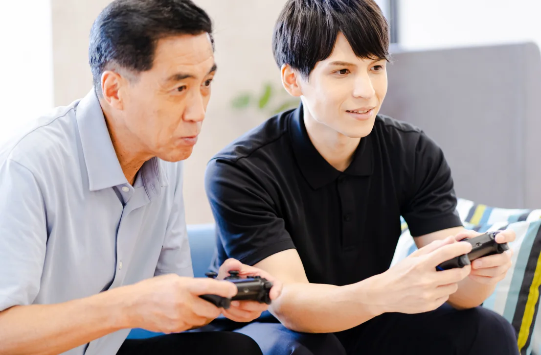 高齢の男性と若い男性がコントローラーを持って一緒に対戦している様子（利用イメージ）