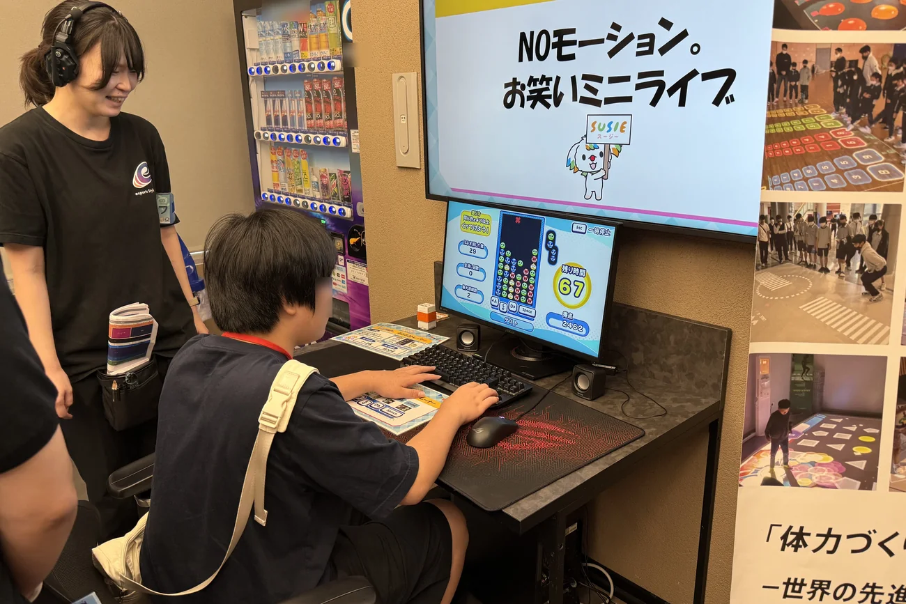 パソコンでぷよぷよトレーナーを体験する参加者と、横で見守る会場スタッフ