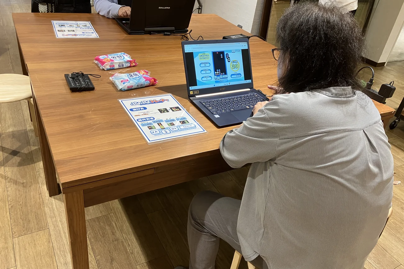 机に置かれた遊び方の案内を前に、ノートパソコンでひとりでぷよぷよを体験する参加者